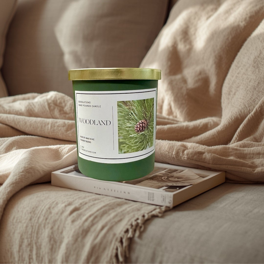 Doodlations Coffee Bar & Boutique Woodland candle in a green jar with a gold lid, featuring a pine cone image.