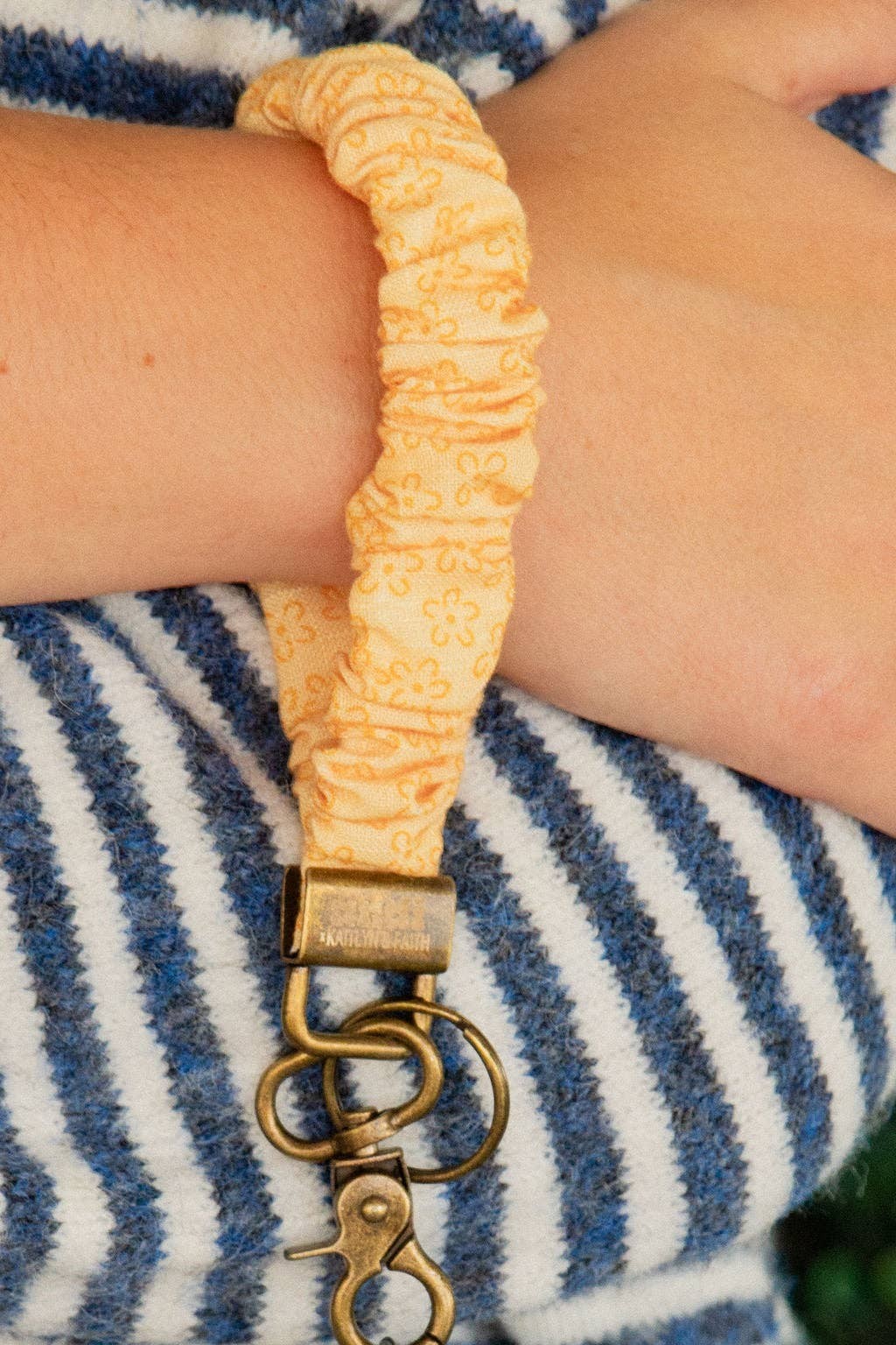 Doodlations Coffee Bar & Boutique yellow floral linen scrunchie keychain worn on a wrist with a striped sweater