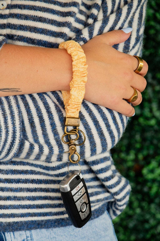 Doodlations Coffee Bar & Boutique yellow floral linen scrunchie keychain worn on a wrist with a car key fob