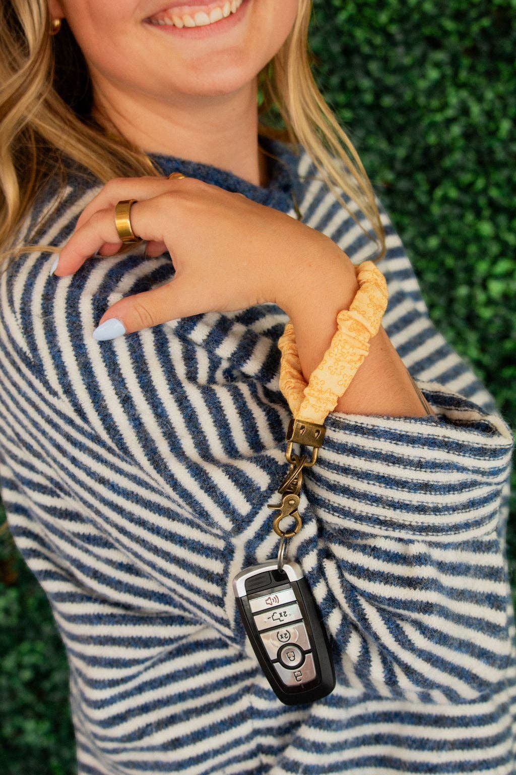 Doodlations Coffee Bar & Boutique yellow floral linen scrunchie keychain worn on a woman's wrist with car keys