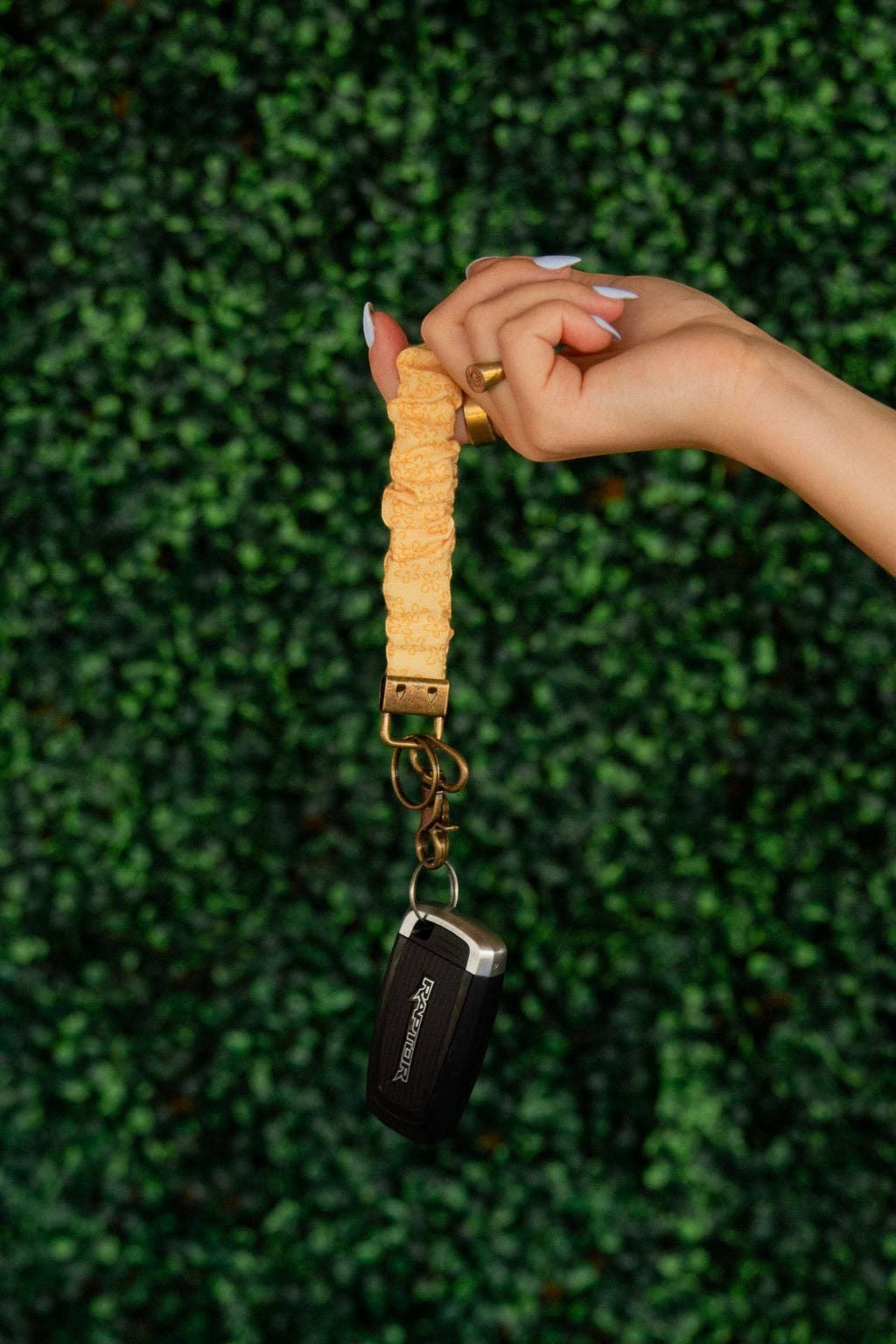 Doodlations Coffee Bar & Boutique Bloom keychain in yellow floral linen held by a hand against a green hedge background