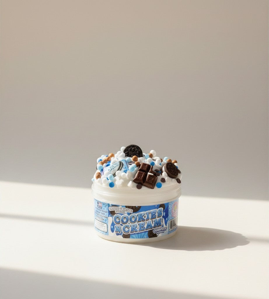 Doodlations Coffee Bar & Boutique Cookies and Cream scented slime in a white tub, topped with chocolate chunks, cookie pieces, and blue sprinkles.