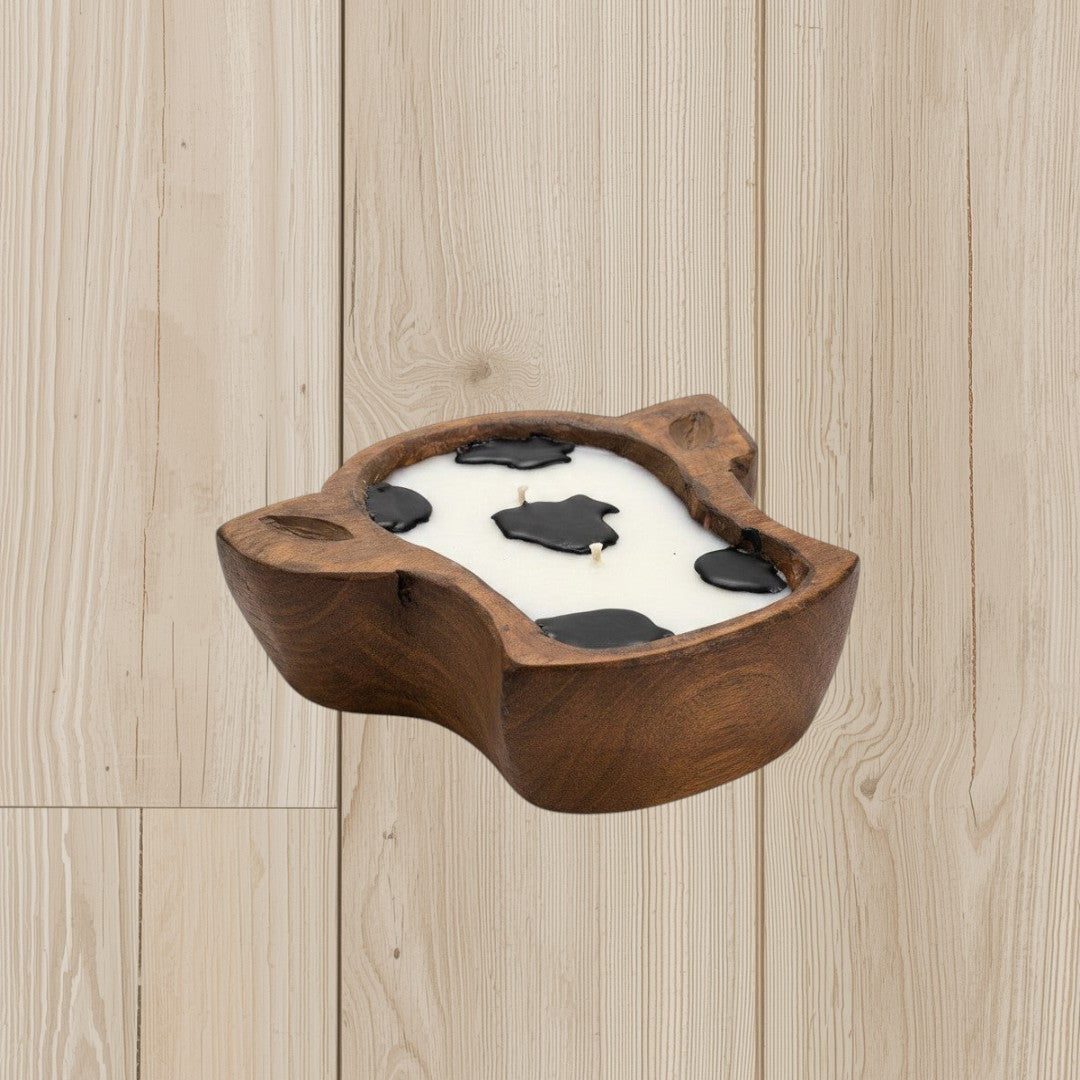 Doodlations wooden dough bowl candle shaped like a cow head with white wax and black cow spots.