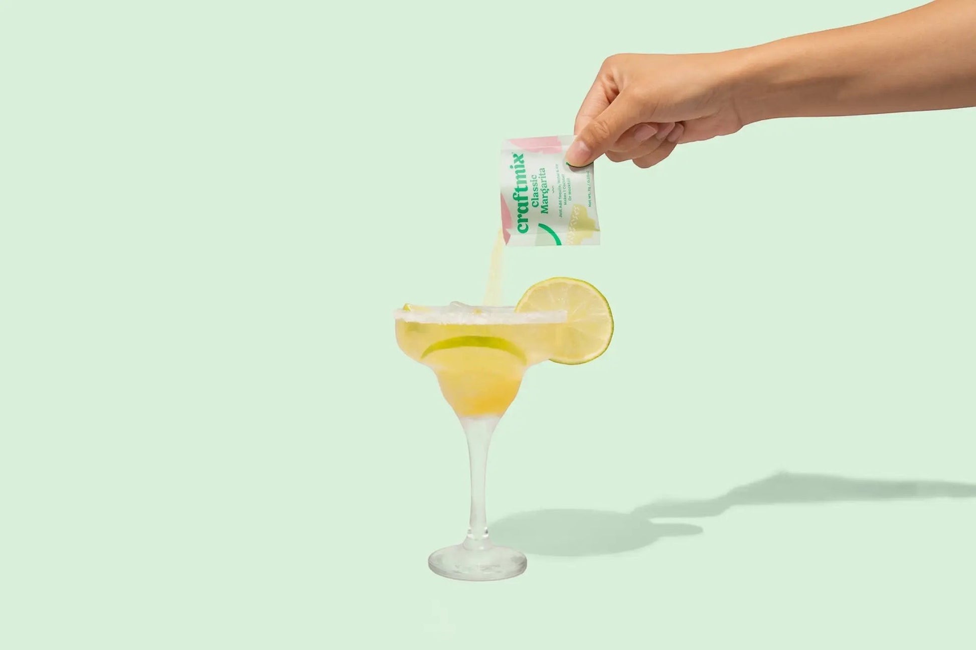 Doodlations Coffee Bar & Boutique Craftmix Classic Margarita mixer packet being poured into a margarita glass with lime and salt rim.