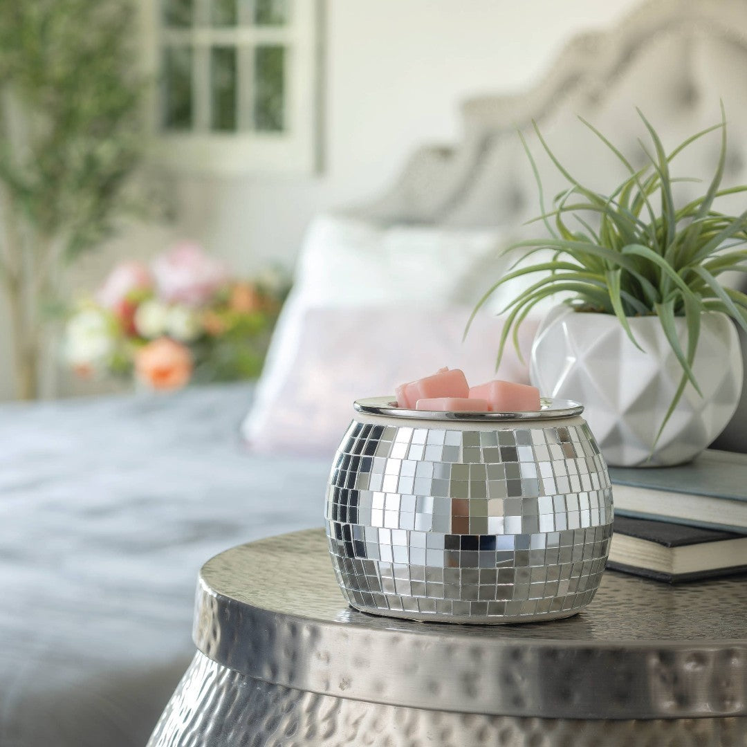 Doodlations disco ball wax warmer with pink wax melts and a silver base, emitting a soft glow.