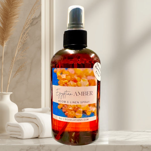 Doodlations Coffee Bar & Boutique Egyptian Amber Room & Linen Spray bottle with amber-colored liquid and a label featuring amber resin pieces.