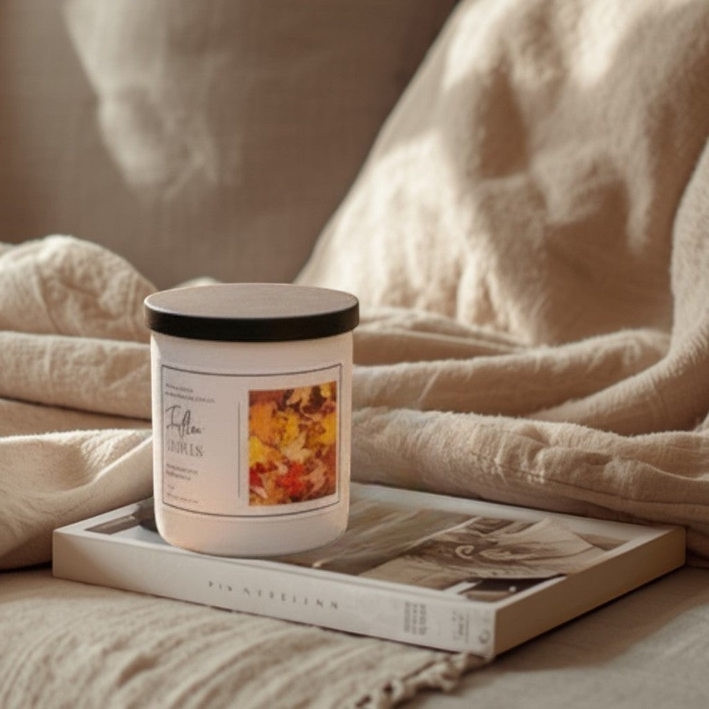 Doodlations Coffee Bar & Boutique Fallen Leaves candle with lid off, emitting smoke, on a wooden table in an autumn forest setting.