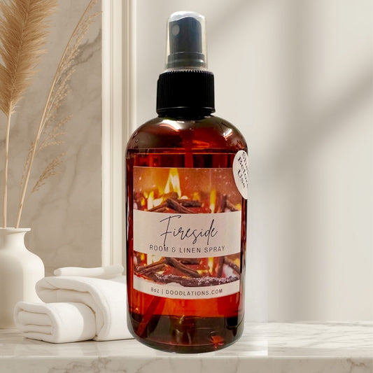 Doodlations Coffee Bar & Boutique Fireside room and linen spray in amber bottle with a cozy fire label. Notes of smoke, wood, clove, amber, sandalwood, and patchouli.