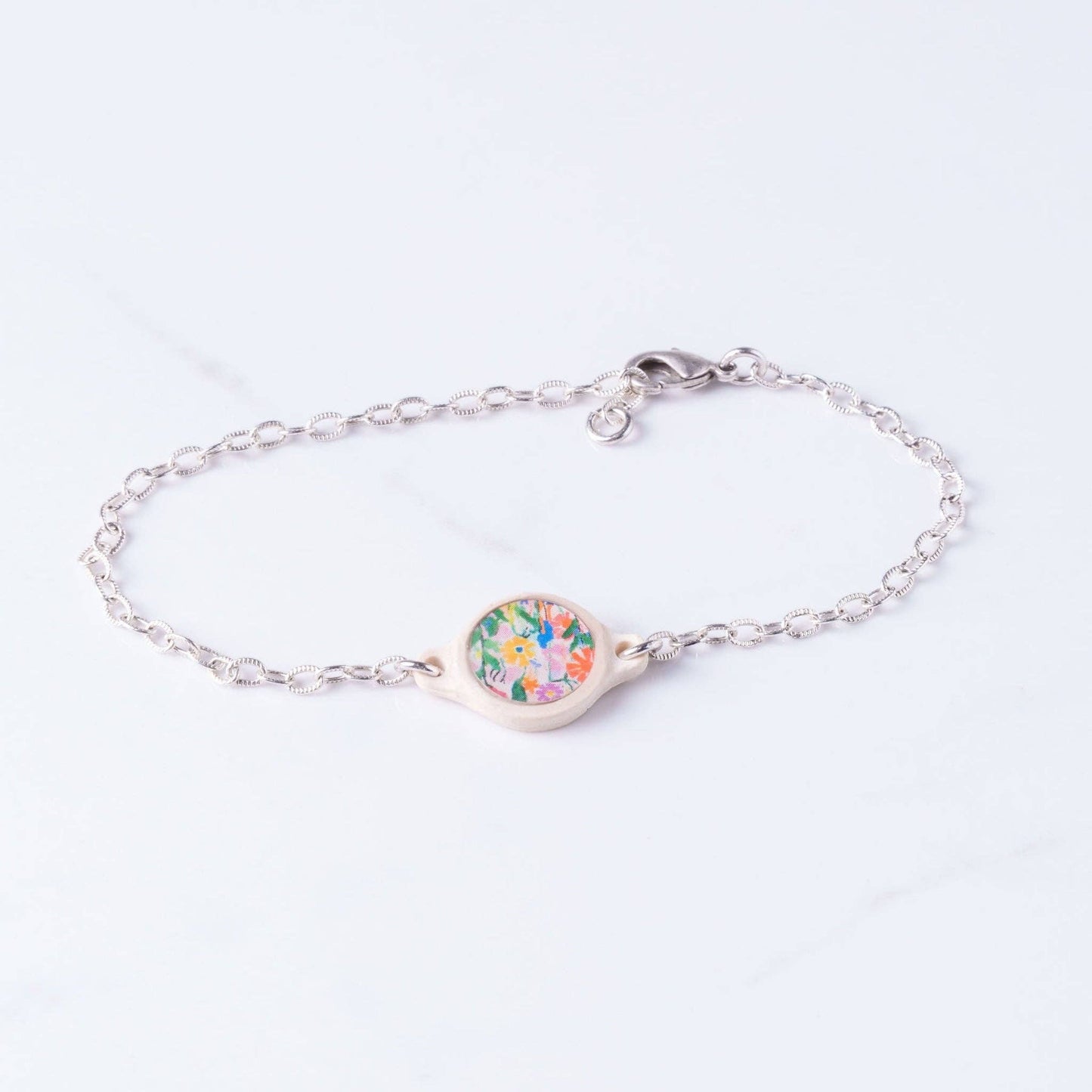 Doodlations Coffee Bar & Boutique silver chain bracelet with a cream-colored charm featuring a colorful floral print.