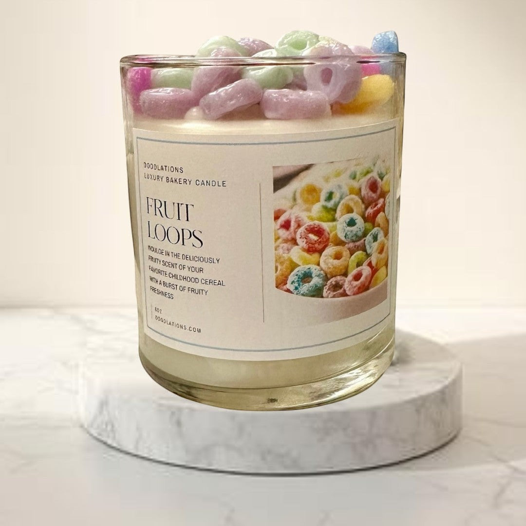 Doodlations Fruit Loops luxury bakery candle in a glass jar, topped with colorful cereal pieces. Scented like fruity cereal and milk.