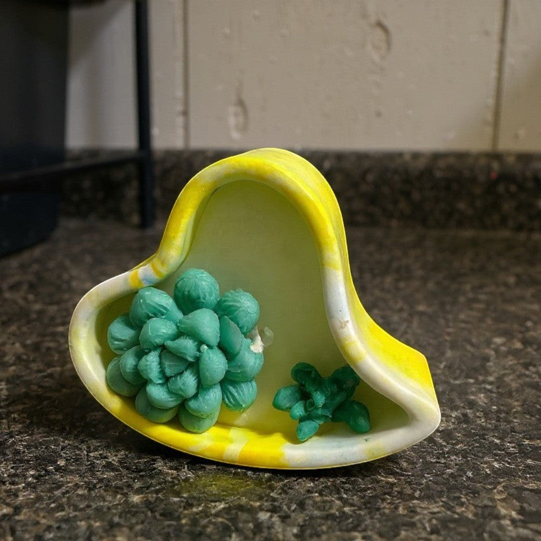 Doodlations yellow and white heart-shaped concrete candle with green succulent wax embeds. Unique interlocking design.