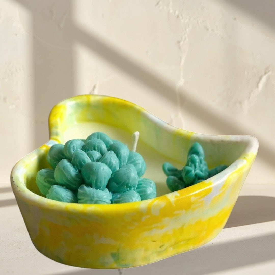 Doodlations heart-shaped concrete candle vessel with yellow marbling, holding a teal succulent-shaped candle.