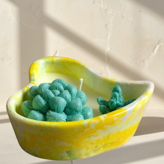 Doodlations heart-shaped concrete candle vessel with yellow marbling, holding a teal succulent-shaped candle.