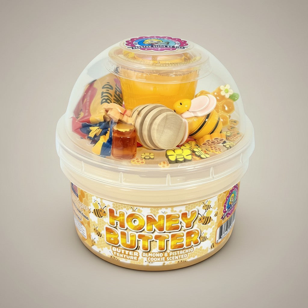 Doodlations Honey Butter slime with a thick, buttery texture, scented with almond and pistachio cookies. Topped with golden drizzle, mini honey dipper, bee charm, and honey-themed sprinkles.