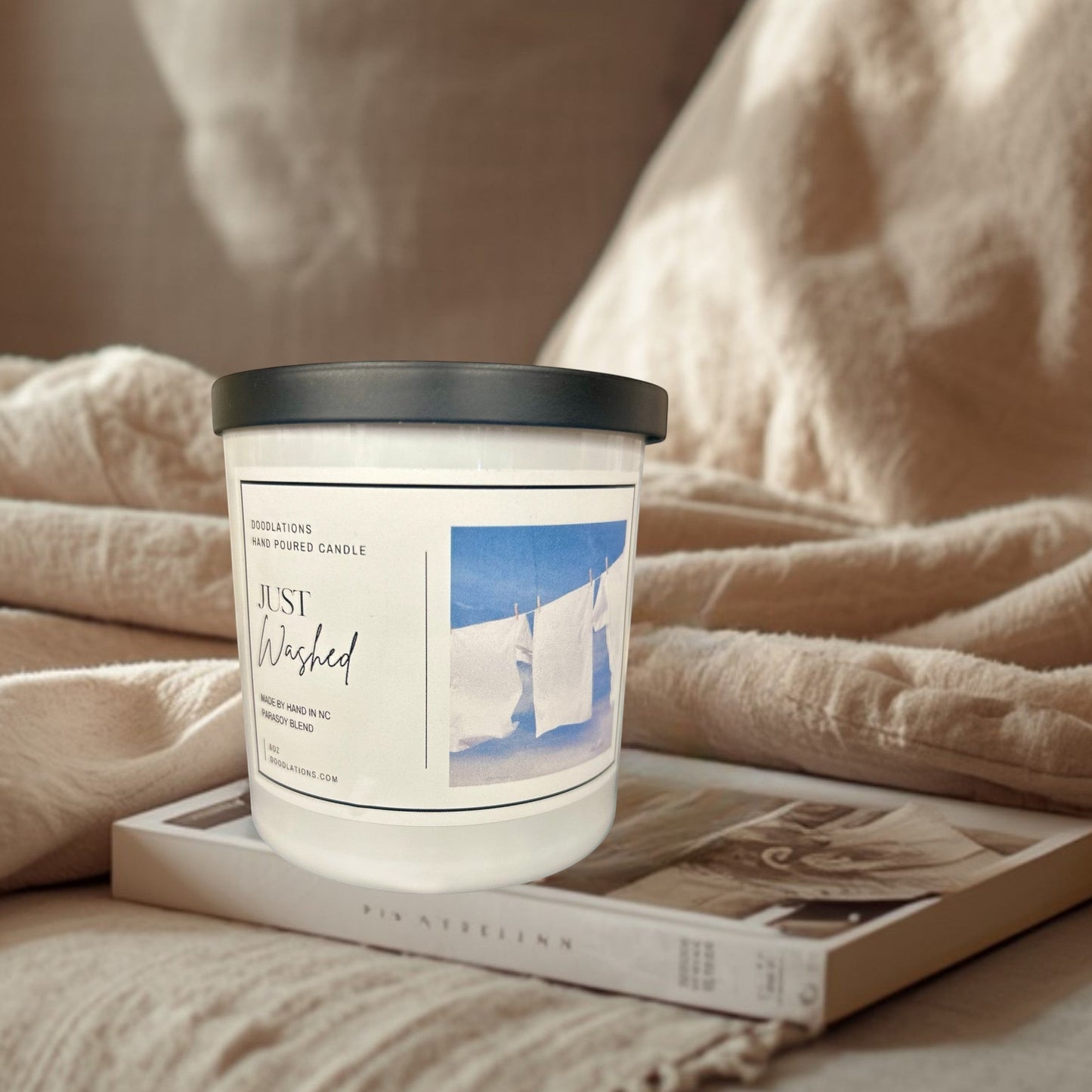 Doodlations Just Washed candle with a clean laundry scent, featuring white sheets drying on a clothesline against a blue sky.