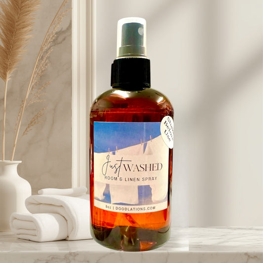 Doodlations Just Washed room and linen spray in amber bottle with black spray top. Scent notes: Mountain Air, Cotton Blossoms, Pink Jasmine, Sandalwood.