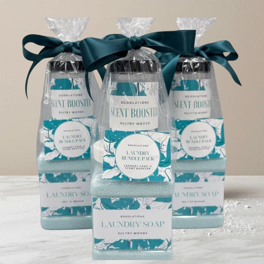 Doodlations Coffee Bar & Boutique Laundry Bundle featuring powdered laundry soap and scent booster in Sultry Woods scent, packaged in clear bottles with teal ribbon.