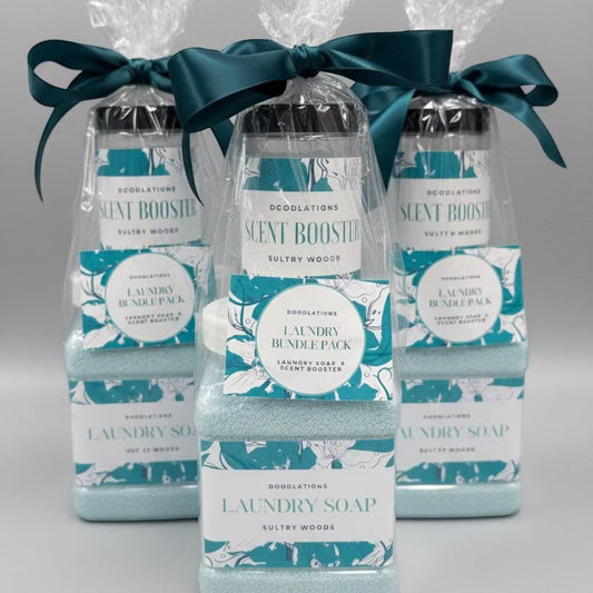 Doodlations Coffee Bar & Boutique Laundry Bundle featuring powdered laundry soap and scent booster in Sultry Woods scent, packaged in clear bottles with teal ribbon.