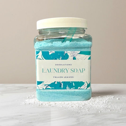 Doodlations Powder Laundry Detergent in Fallen Leaves scent, a bright blue powder in a clear plastic jar with a white lid.