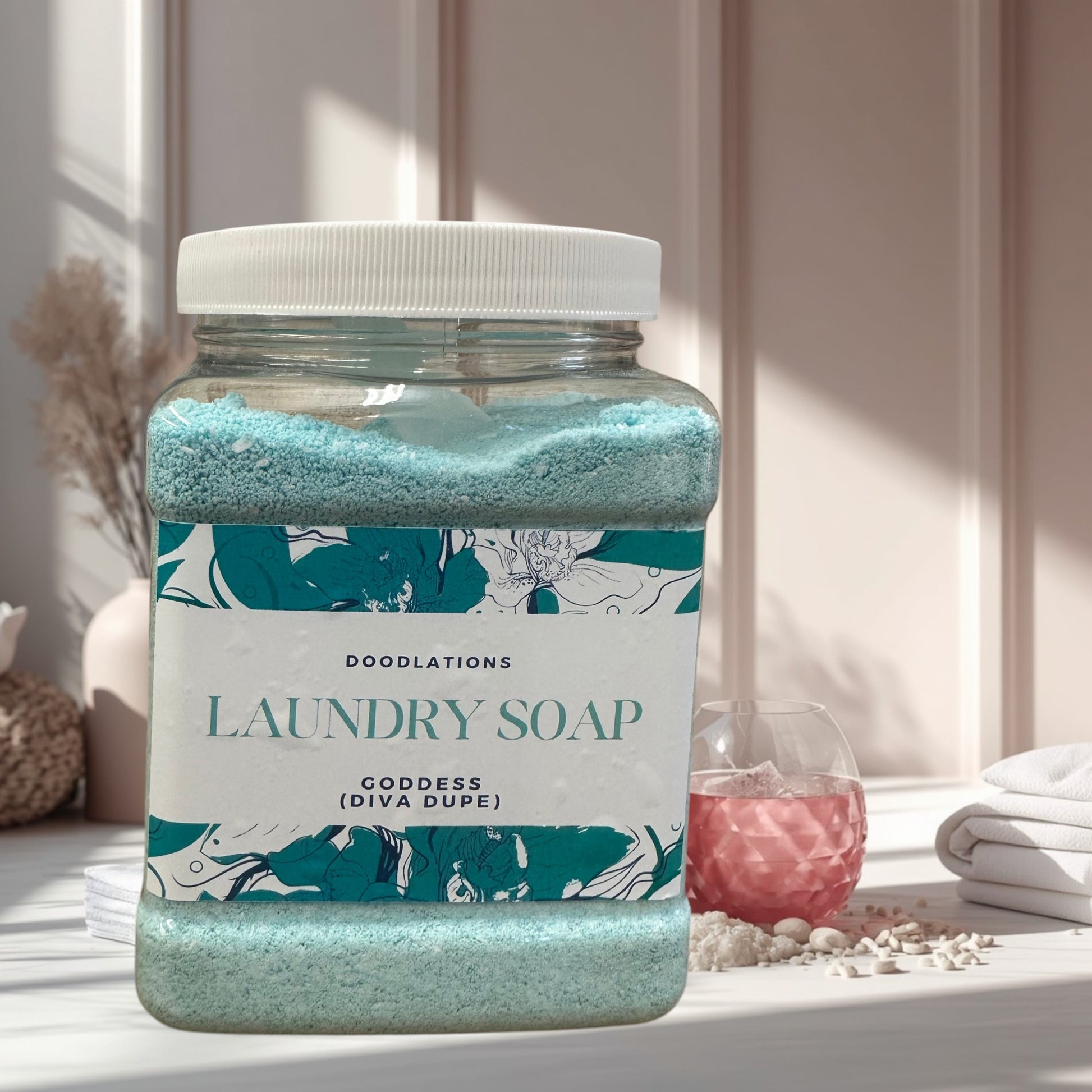 Doodlations Goddess luxury laundry powder in a clear jar with a white lid. Blue powder with floral label.