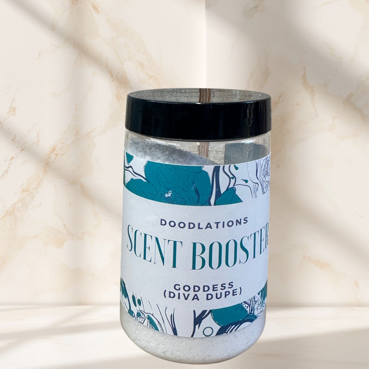 Doodlations Laundry Scent Booster in Goddess scent, a clear jar filled with white granules, on a shelf with pink towels.