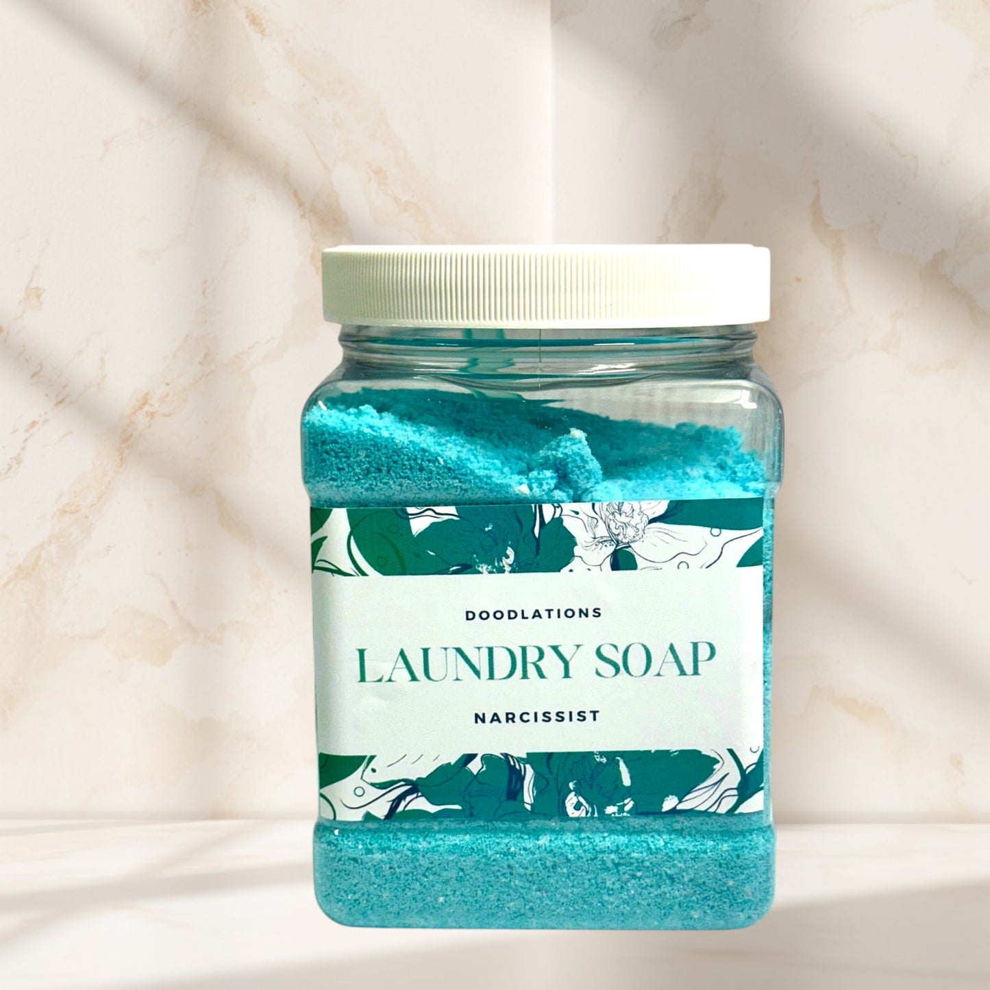 Doodlations Narcissist luxury laundry soap powder in a clear jar with a white lid. Blue powder with floral label.