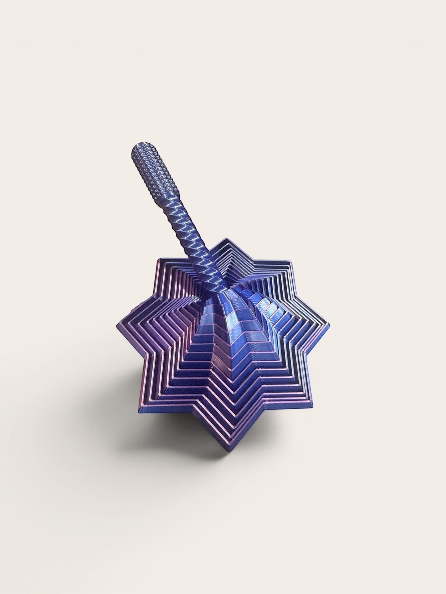 Doodlations Coffee Bar & Boutique Layered Star Fidget Toy in iridescent blue metal with rotating segments for stress relief.