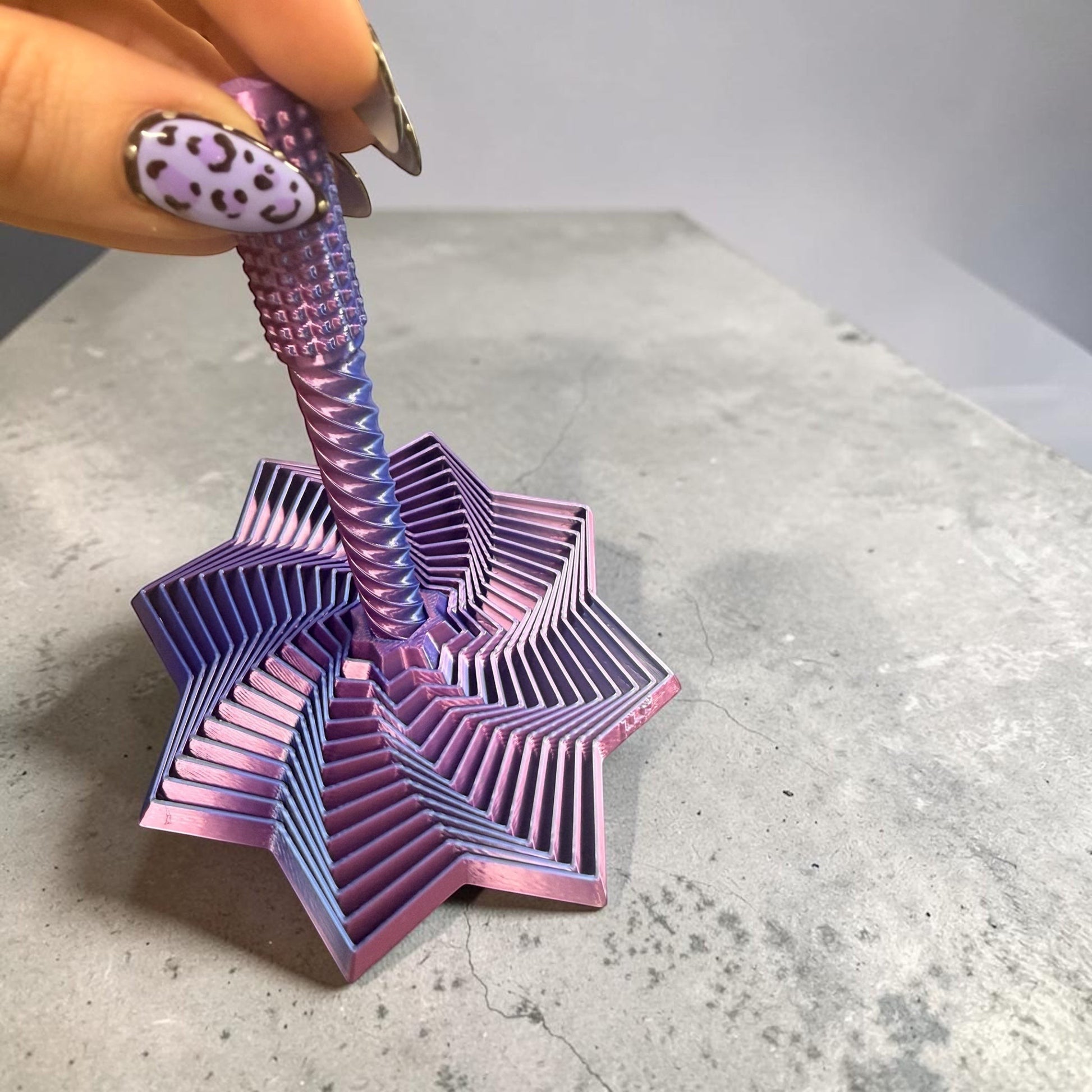 Doodlations Coffee Bar & Boutique Layered Star Fidget Toy, iridescent purple and pink metal, with rotating interlocking segments for stress relief.
