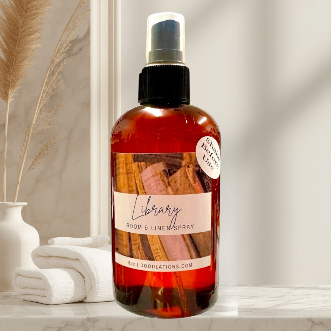 Doodlations Coffee Bar & Boutique Library room and linen spray in amber bottle with wood spine label. Notes of teakwood, cedar, leather, sandalwood, musk, patchouli.