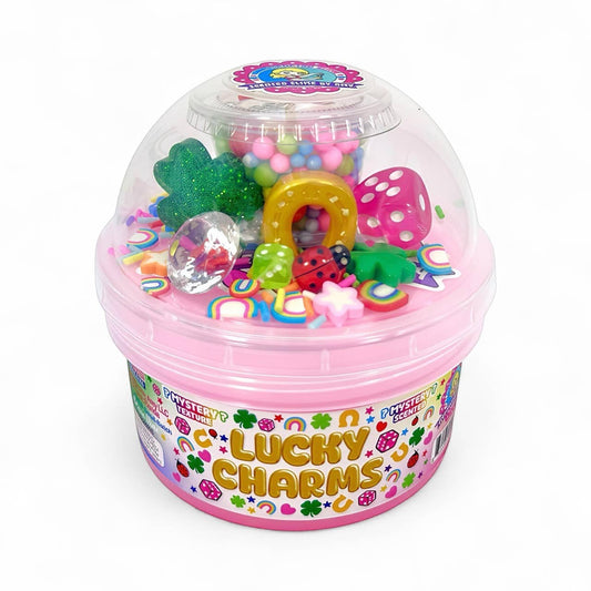 Doodlations Lucky Charms mystery slime in a pink container with a clear dome lid, filled with colorful charms like dice, ladybugs, shamrocks, and rainbows.