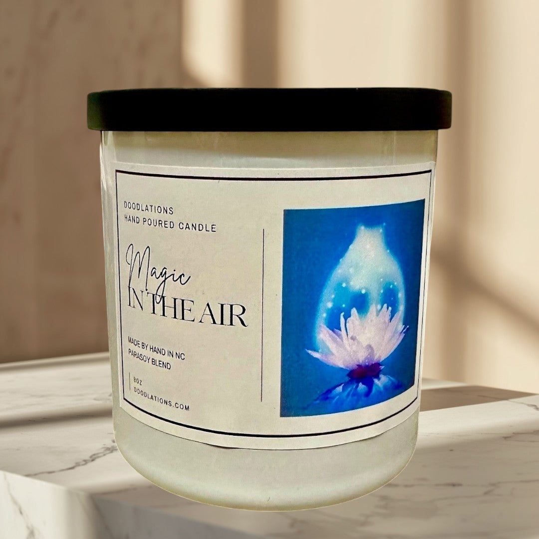 Doodlations Magic in the Air hand-poured soy blend candle with a black lid, featuring floral and citrus notes.