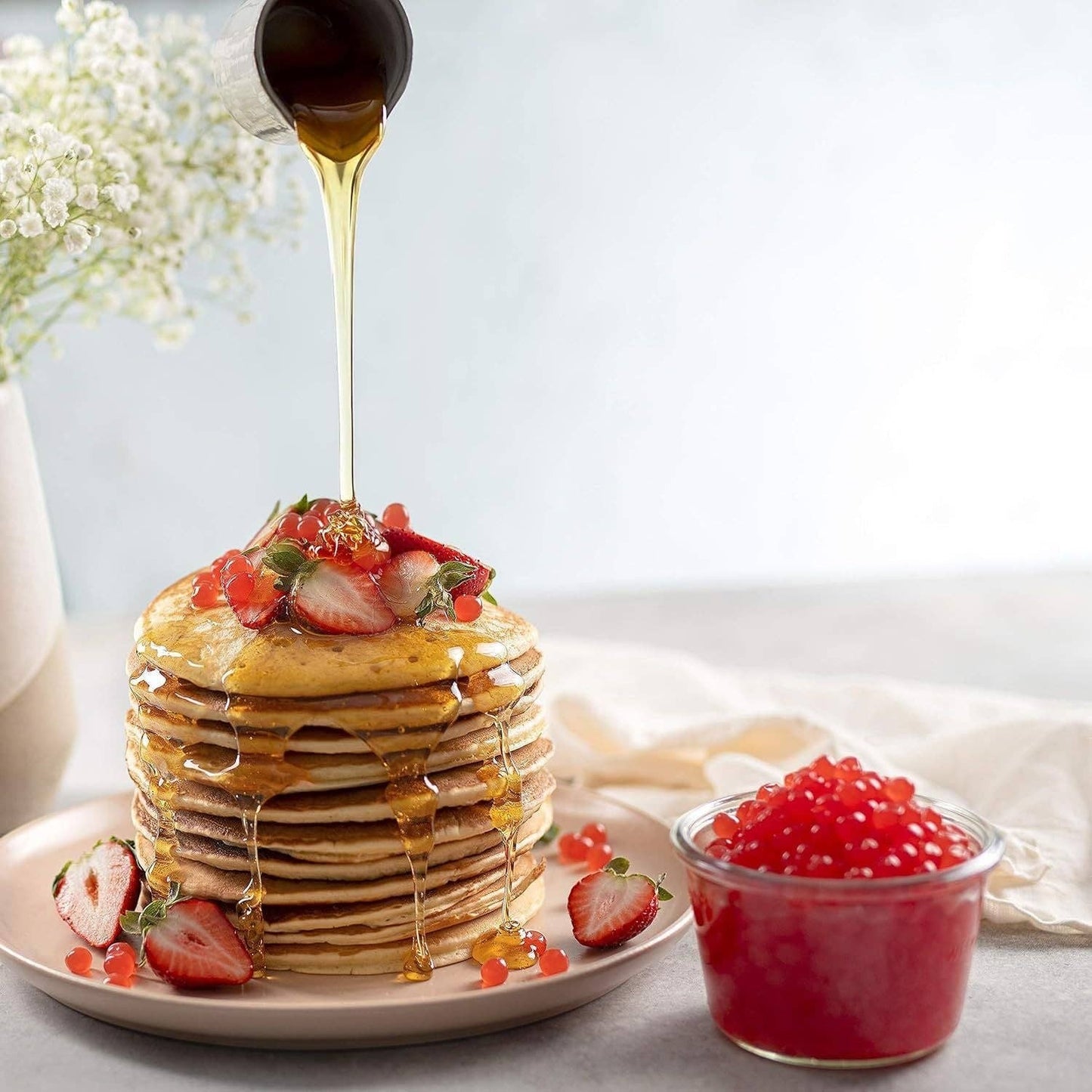 Doodlations Coffee Bar & Boutique Bursting Mango Balls topping a stack of pancakes with strawberries and syrup.