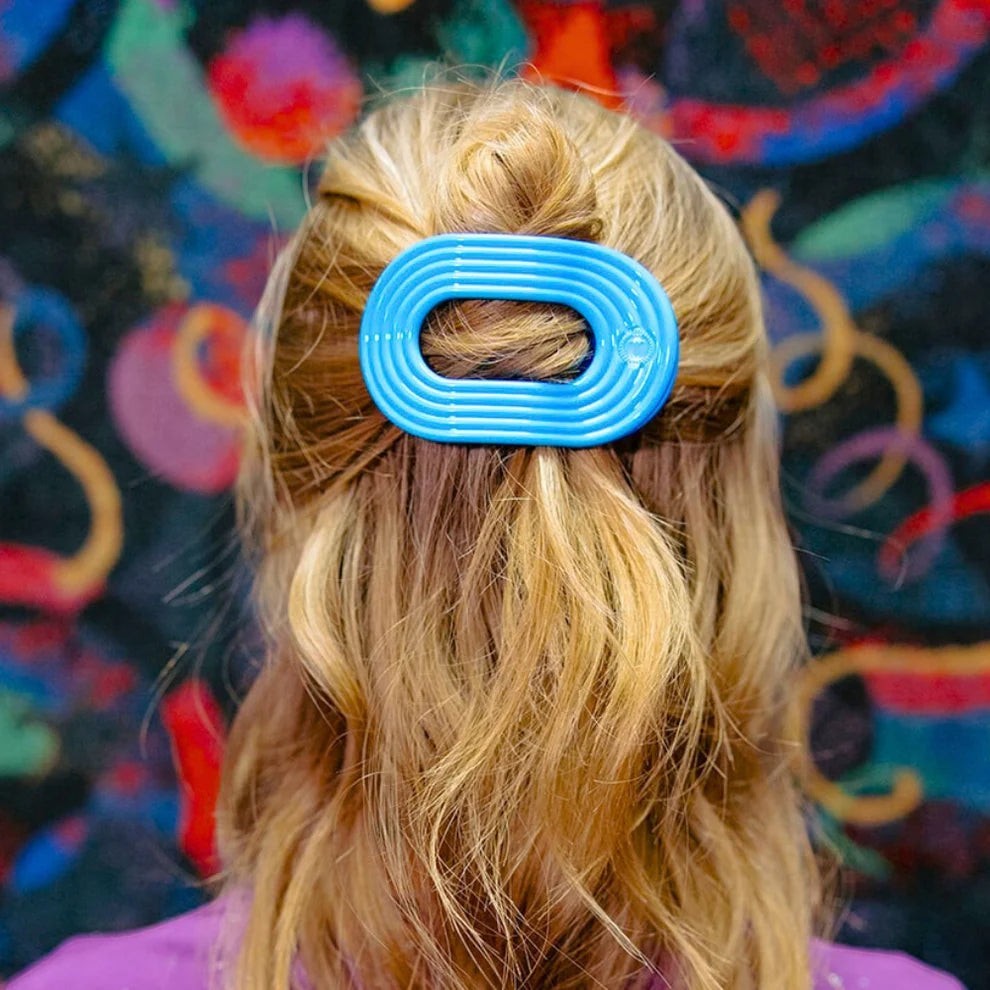 Doodlations Coffee Bar & Boutique blue flat round hair clip with ribbed texture, securing blonde hair in a bun.