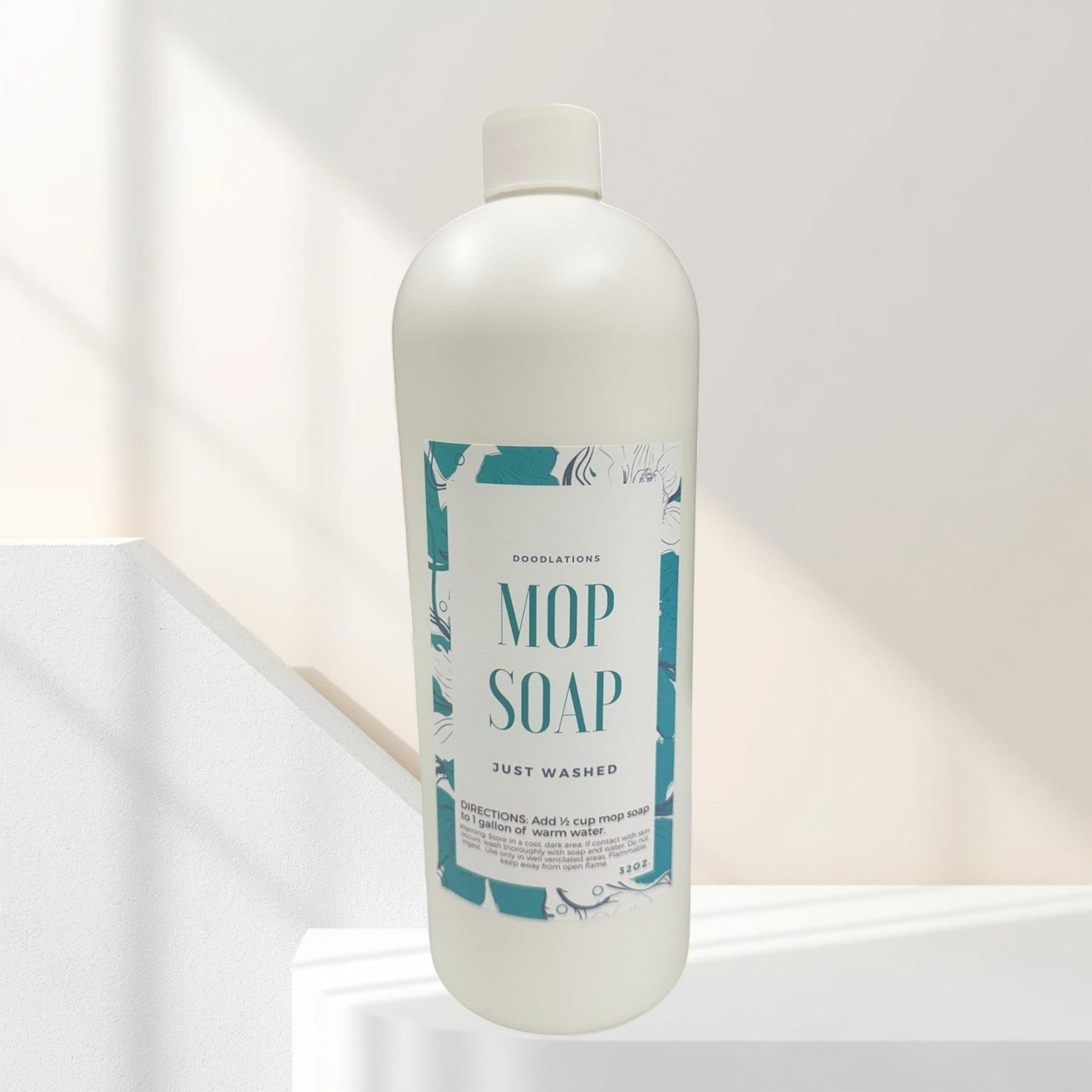 Doodlations Mop Soap, concentrated floor cleaner in a white bottle with a teal floral label, next to a gold mop.