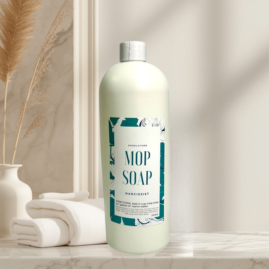 Doodlations Concentrated Mop Soap in The Narcissist scent, a creamy white liquid in a 32 oz bottle with a teal and white label.