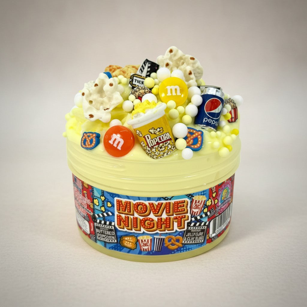 Doodlations Movie Night yellow jelly cube clay slime with popcorn, M&Ms, Pepsi can, and movie ticket charms.