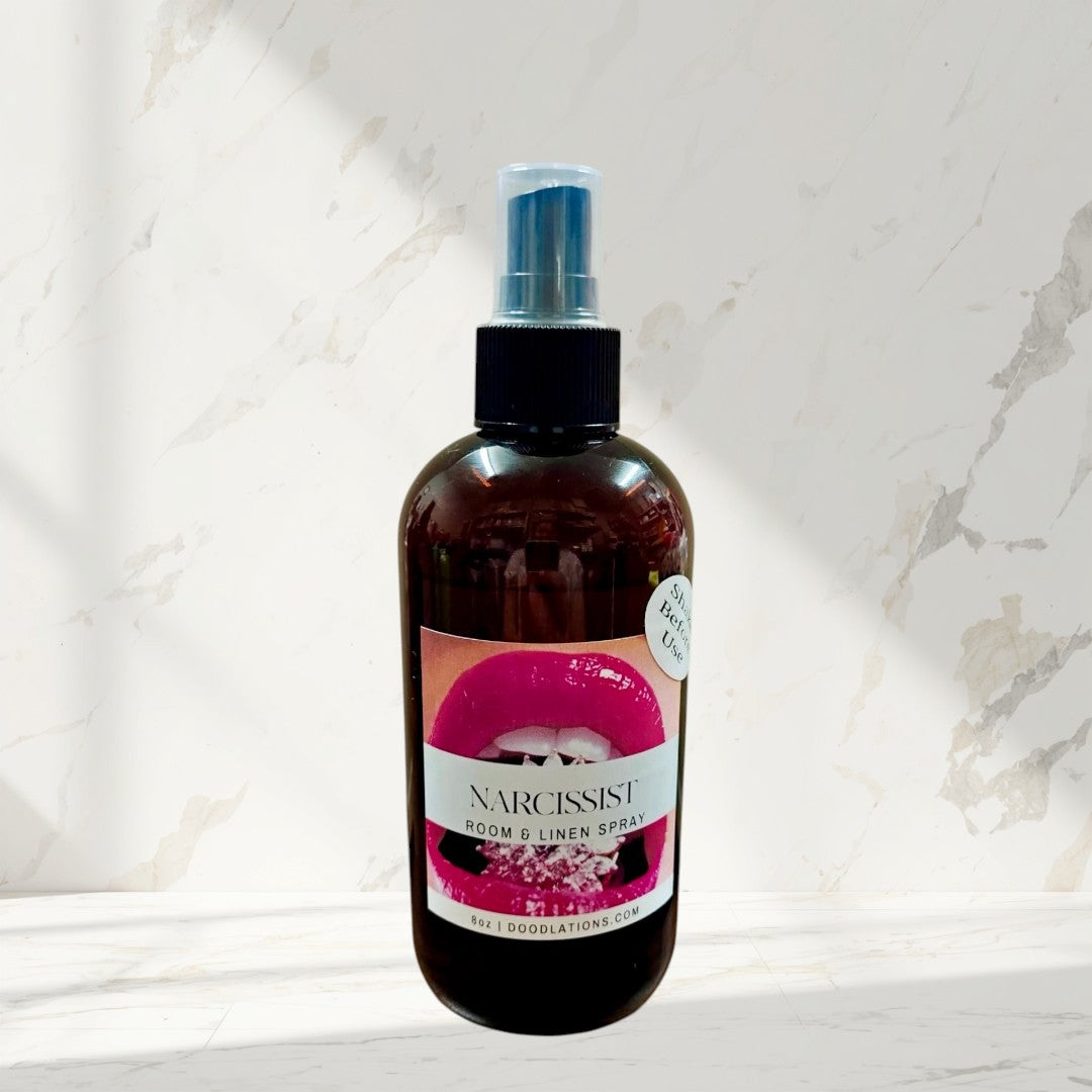 Doodlations Narcissist room & linen spray in amber bottle with bold pink lips label. Fruity-floral scent.