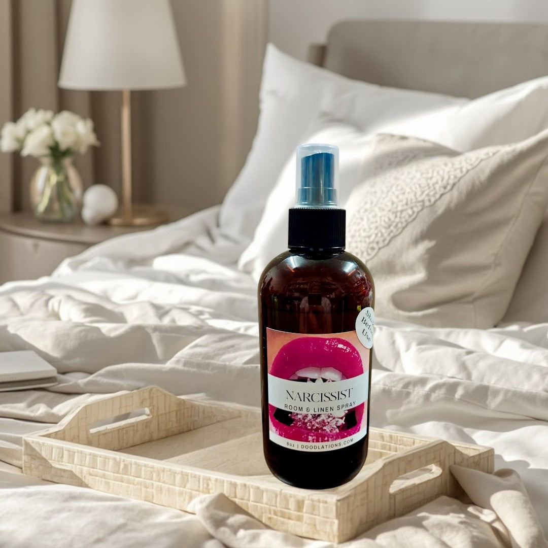 Doodlations Narcissist room and linen spray in a brown glass bottle with a pink lips label. Fruity-floral scent.
