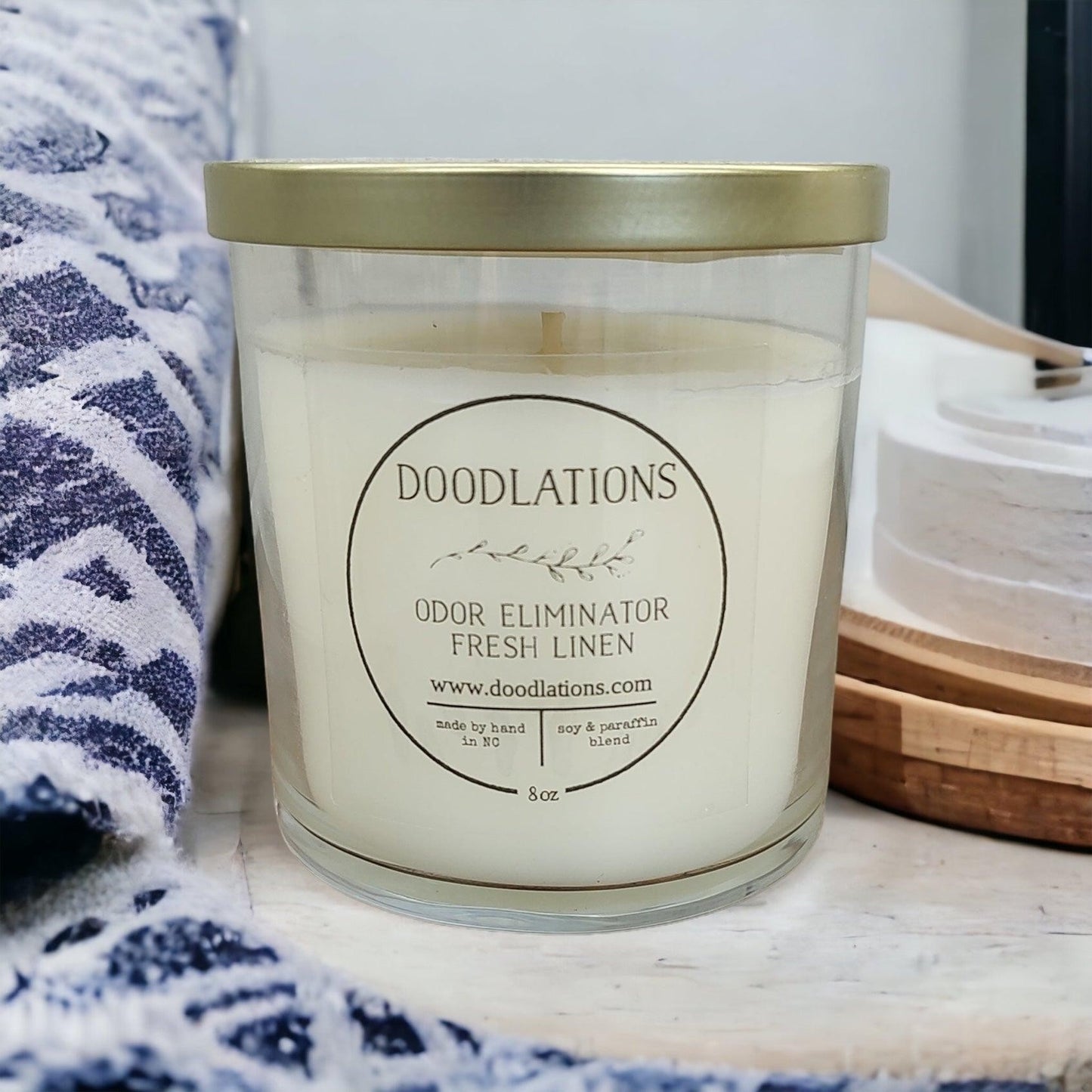 Doodlations Odor Eliminator Fresh Linen candle in a clear glass jar with a gold lid. Soy and paraffin blend.
