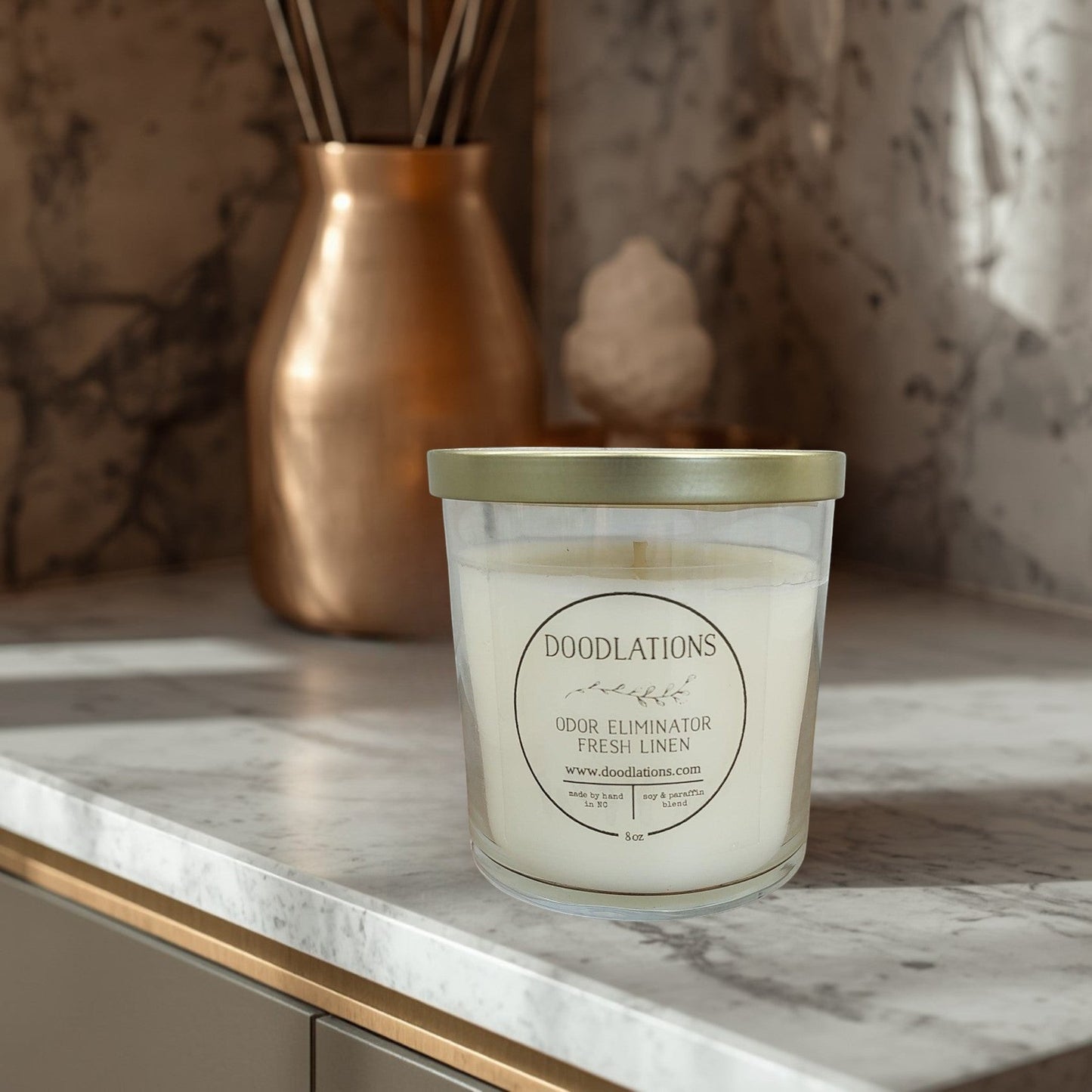 Doodlations Odor Eliminator Fresh Linen candle in a clear glass jar with a gold lid. Soy and paraffin blend.