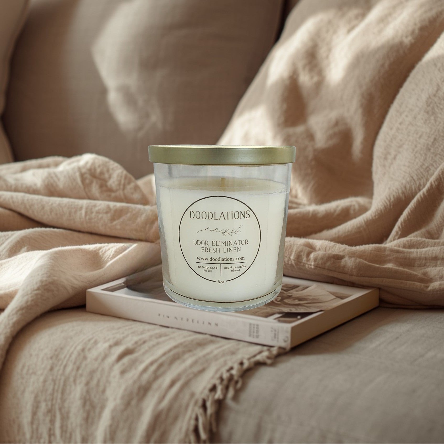 Doodlations Odor Eliminator Fresh Linen candle in a clear glass jar with a gold lid. Soy & paraffin blend.
