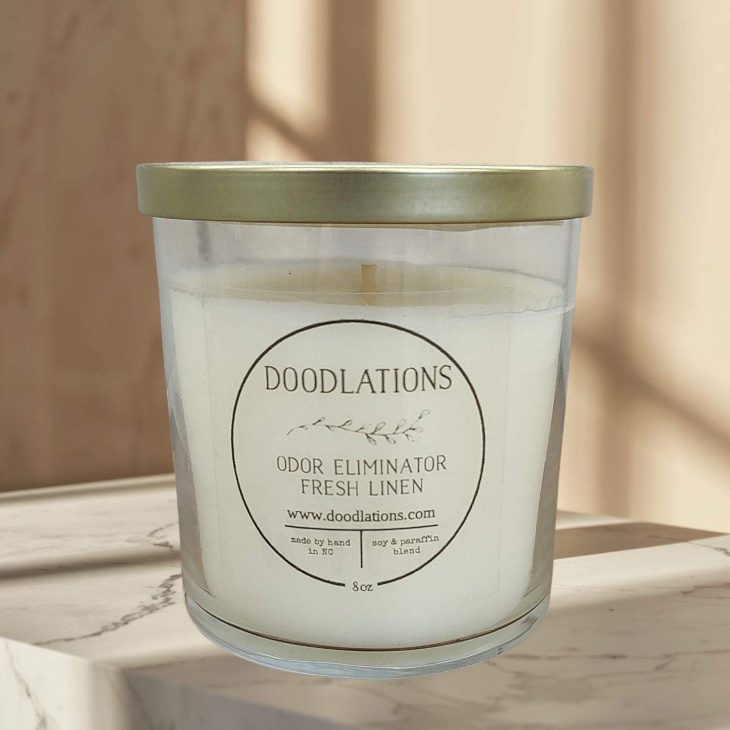 Doodlations Odor Eliminator Fresh Linen candle in a clear glass jar with a gold lid. Soy & paraffin blend.