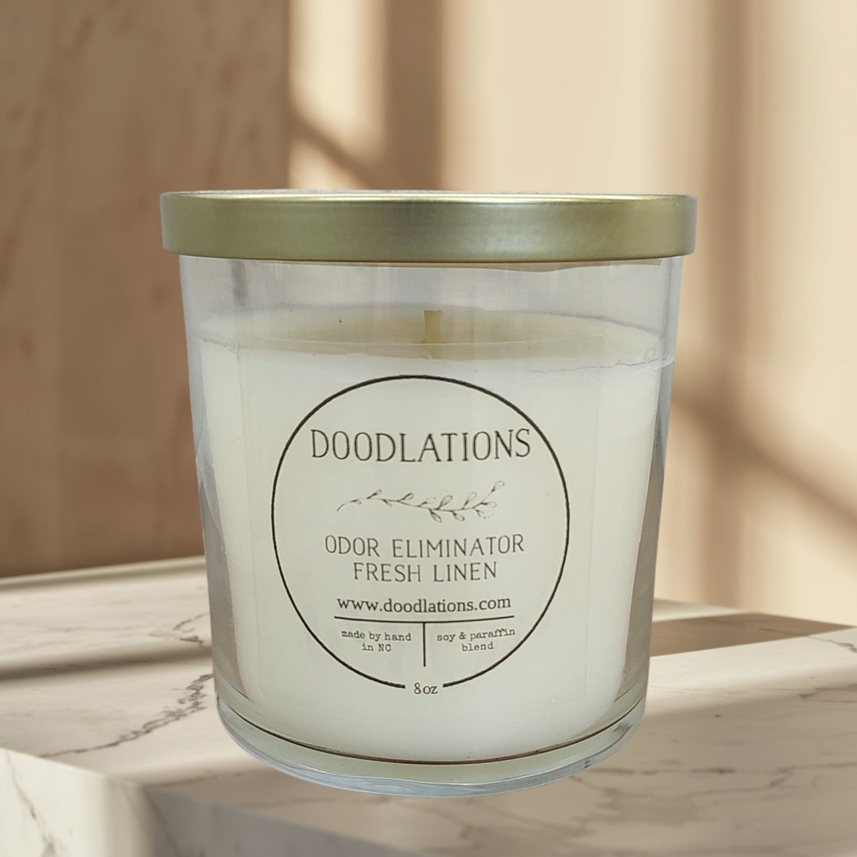 Doodlations Odor Eliminator Fresh Linen candle in a clear glass jar with a gold lid. Soy & paraffin blend.