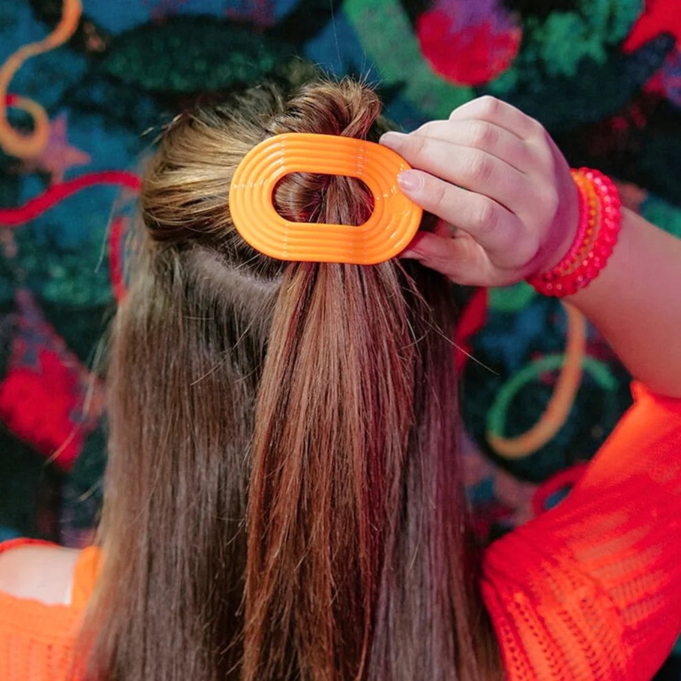 Doodlations Coffee Bar & Boutique orange oval hair clip with ribbed texture, holding back hair.