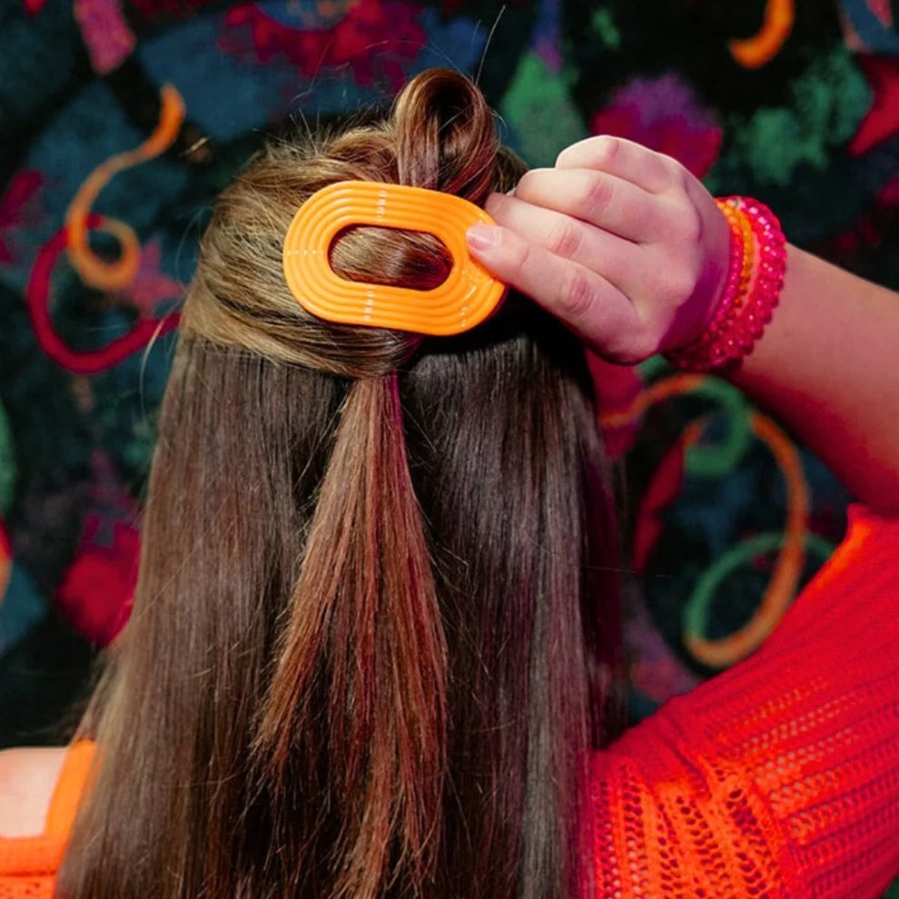 Doodlations Coffee Bar & Boutique orange flat round Teleties hair clip holding back hair. Durable material for styling.
