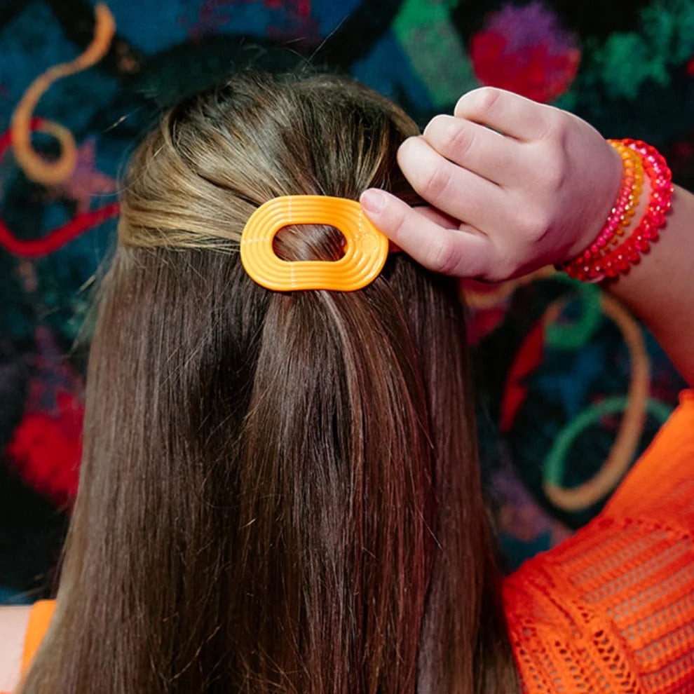 Doodlations Coffee Bar & Boutique orange oval hair clip with ribbed texture, securing brown hair.