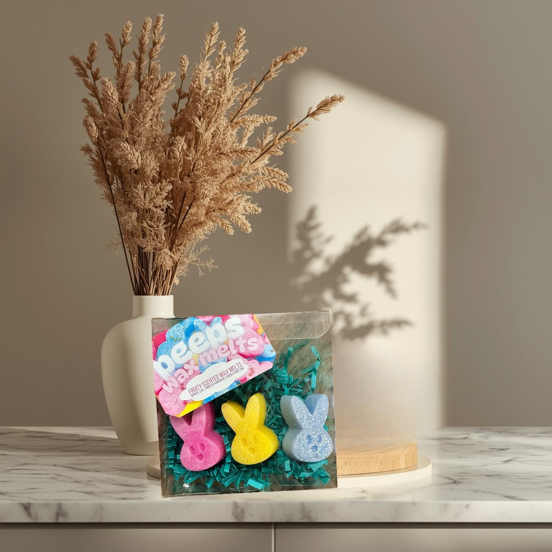Doodlations Peeps wax melts in pink, yellow, and blue bunny shapes with glitter, nestled in green crinkle paper.