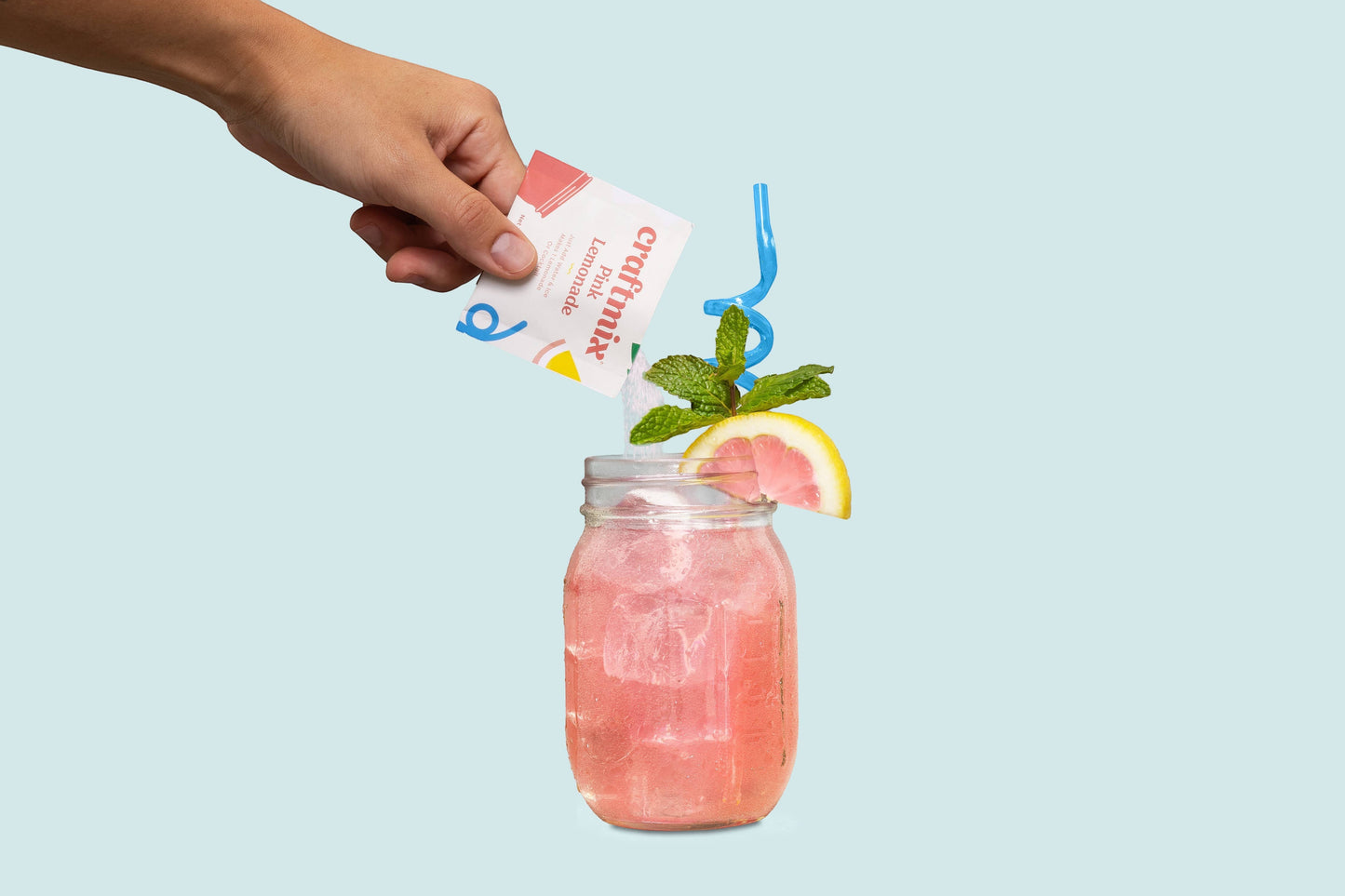 Doodlations Coffee Bar & Boutique Pink Lemonade drink mix packet being poured into a glass of pink lemonade with ice, lemon slice, and mint.