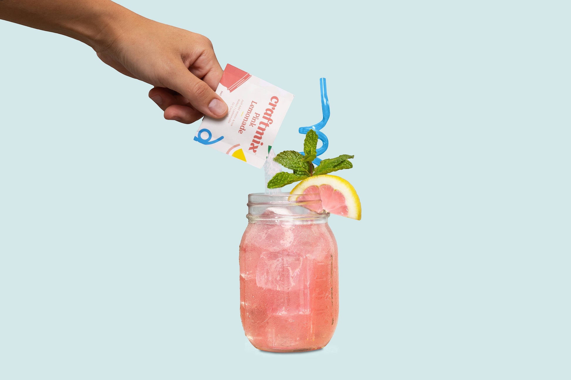 Doodlations Coffee Bar & Boutique Pink Lemonade drink mix packet being poured into a glass of pink lemonade with ice, lemon slice, and mint.