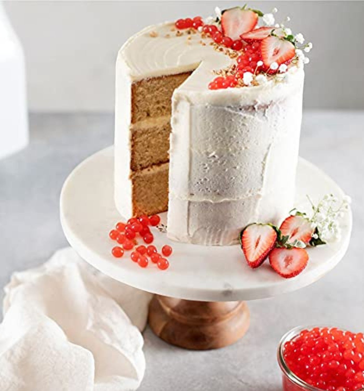 Doodlations Coffee Bar & Boutique Pomegranate Bursting Balls topping a white frosted cake with strawberries and baby's breath.